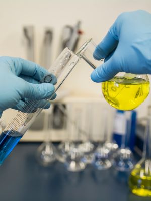 a scientist with gloves on pouring a solution from a beaker into a test tube