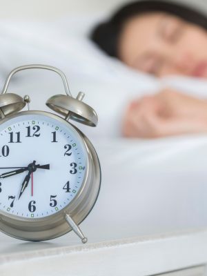 woman asleep in bed with her alarm clock on the bedside table