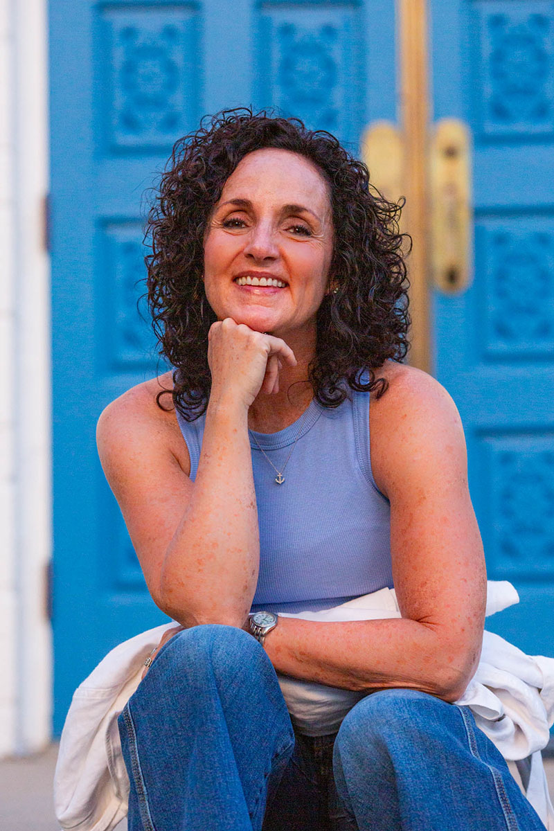 Julie James, FDNP sitting in front of a bright blue door, smiling
