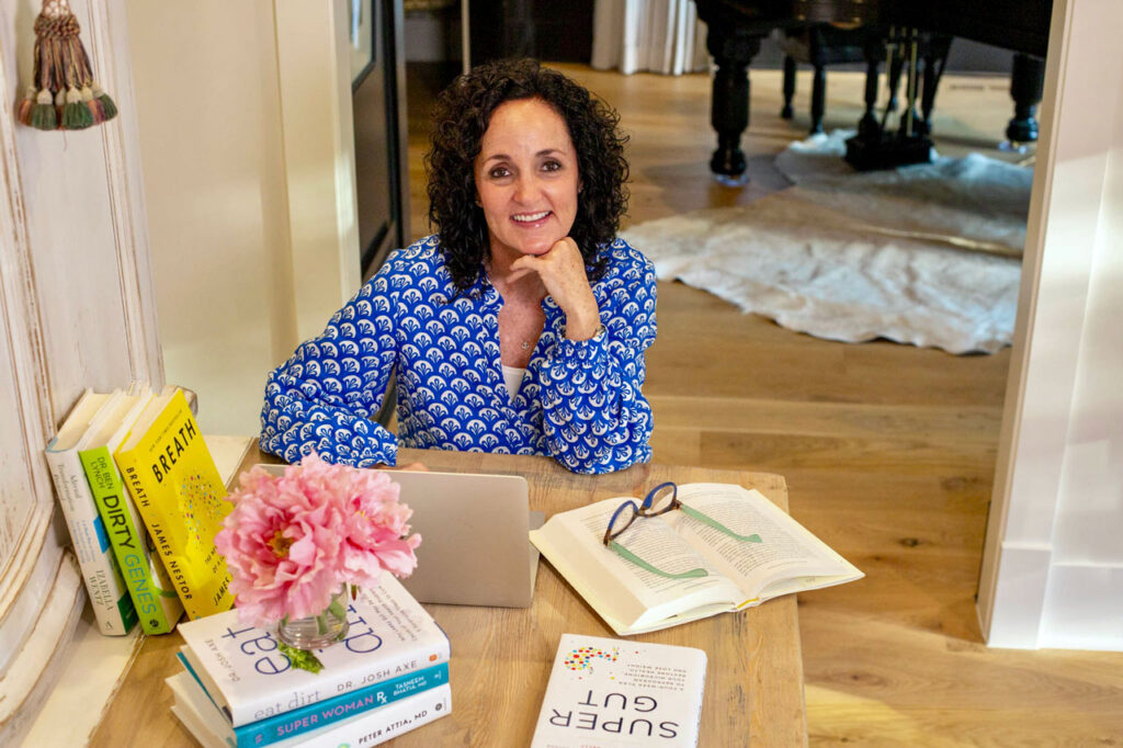 Julie James FDNP working at her laptop computer, surround by functional health and wellness books