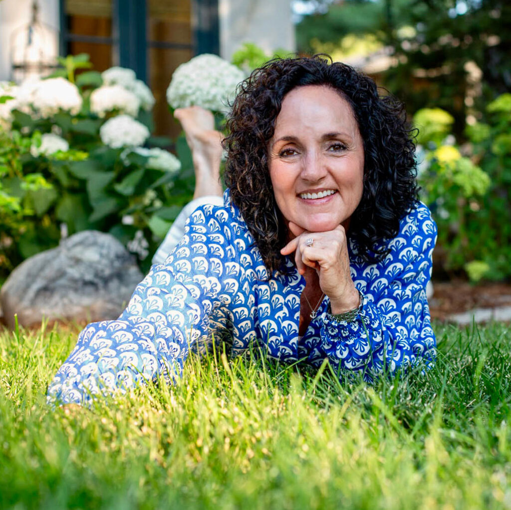 Julie James, functional health practitioner lying in the lush green grass and enjoying the health effects of grounding in nature