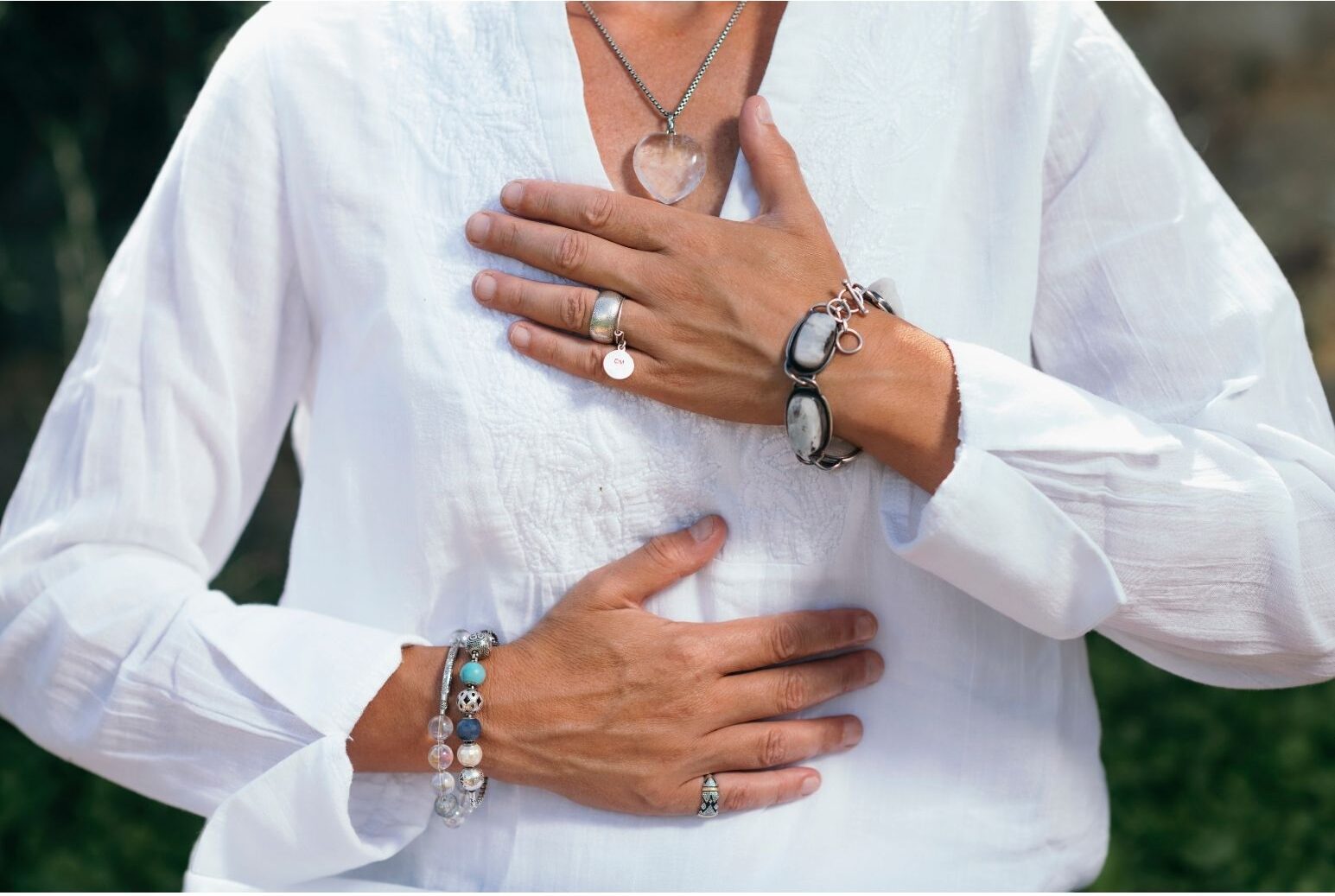 a woman practicing deep breathing, sitting with one hand on her chest and one on her belly, wearing bracelets and silver jewelry