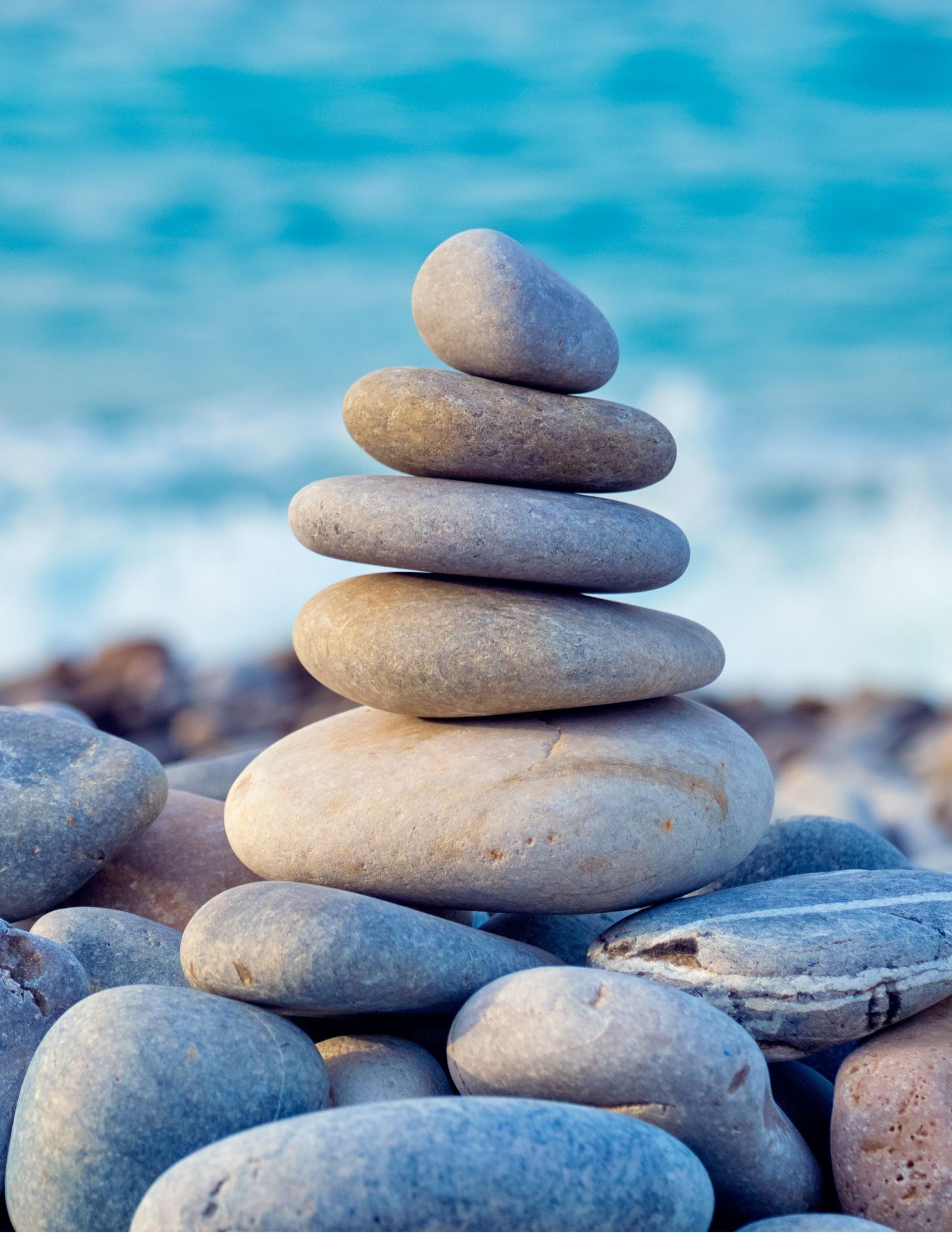 a stack of smooth rocks delicatley balanced on top of each other, positioned in front of a vast blue water
