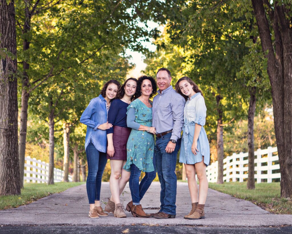 Julie James with her husband and family together standing under a canopy of trees