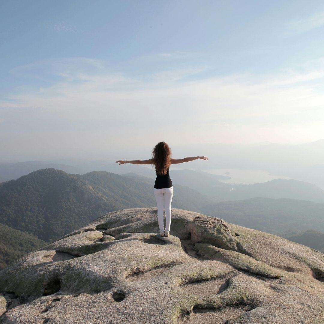 Woman standing at the summit of a mountain top exhilirated by her accomplishment of climbing the mountain