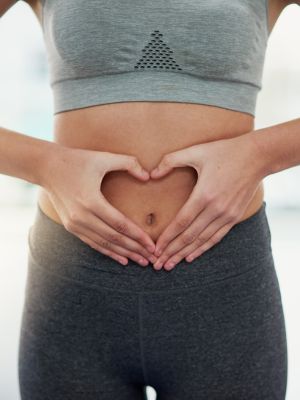 woman in yoga wear with her hands on her belly, thinking about her digestive health